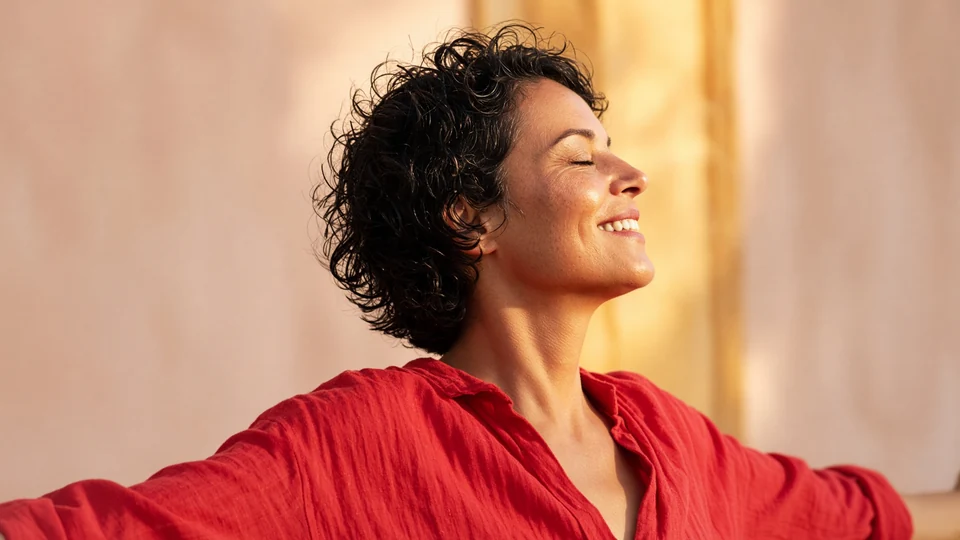An adult woman in a red shirt smiles with her face turned towards the light.